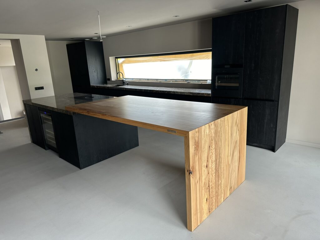 Moderne eikenhouten tafel, geïntegreerd met een donker keukeneiland in een keuken met strakke, grijze vloer.