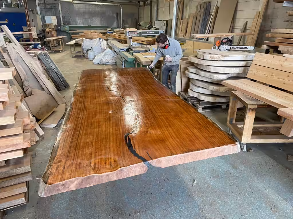 Imposante Mahoniehouten Tafel met Glanzende Afwerking Imposante mahoniehouten tafel met een diepe, warme kleur, glanzende afwerking, natuurlijke rand en opvallende nerfpatronen in een werkplaatsomgeving