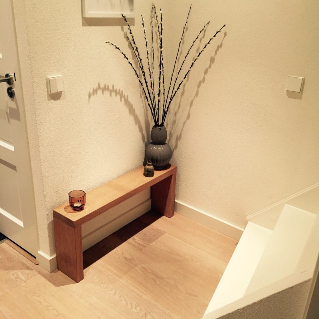Minimalistische eikenhouten side table met een lichte, natuurlijke afwerking, geplaatst in een hoek van een kamer met decoratieve items zoals vazen en kaarsen.